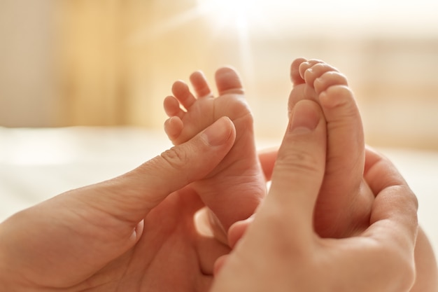Free photo mum making baby massage, mother massaging infant bare foot, preventive massage for newborn, mommy stroking the baby's feet with both hands on light background.