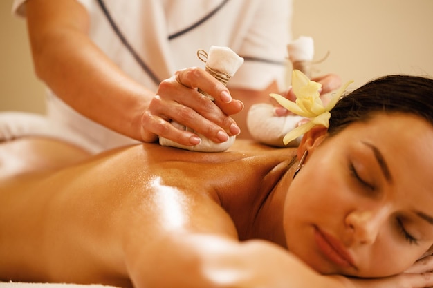 Closeup of relaxed woman getting back massage with herbal balls at health spa