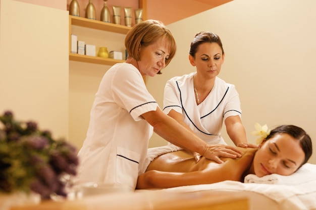 Free photo serene woman getting back massage by two therapists during spa treatment