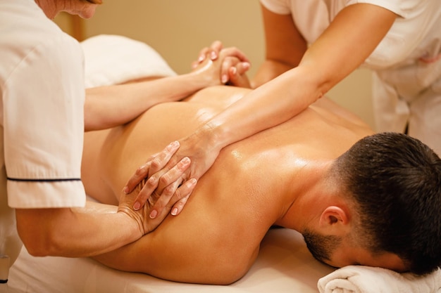 Free photo unrecognizable massage therapists massaging together man's back at health spa