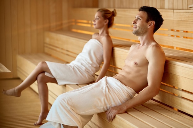 Serene couple relaxing in sauna while spending their weekend at health spa Focus is on man